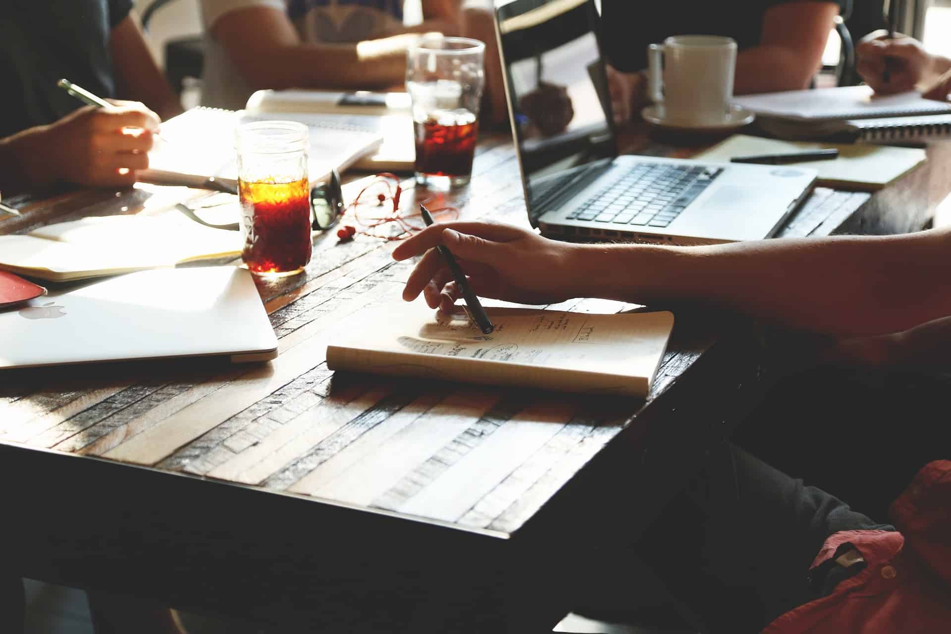 People sitting around a table covered in papers, laptops, and coffee cups